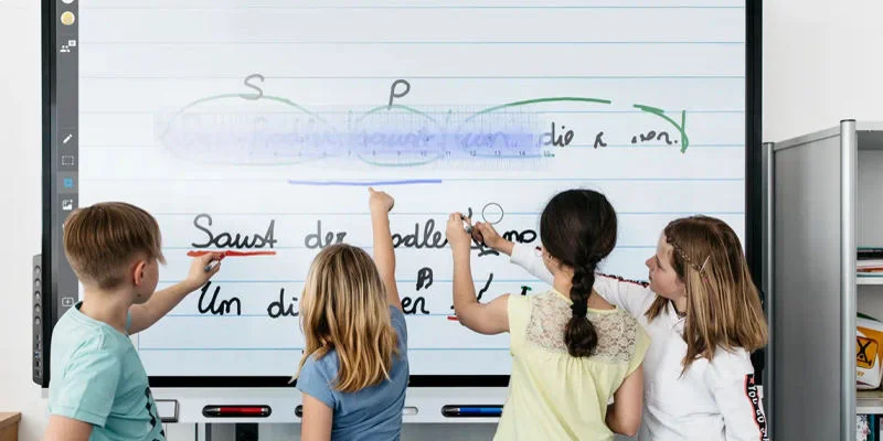 Quatre enfants qui écrivent sur un écran interactif smart.